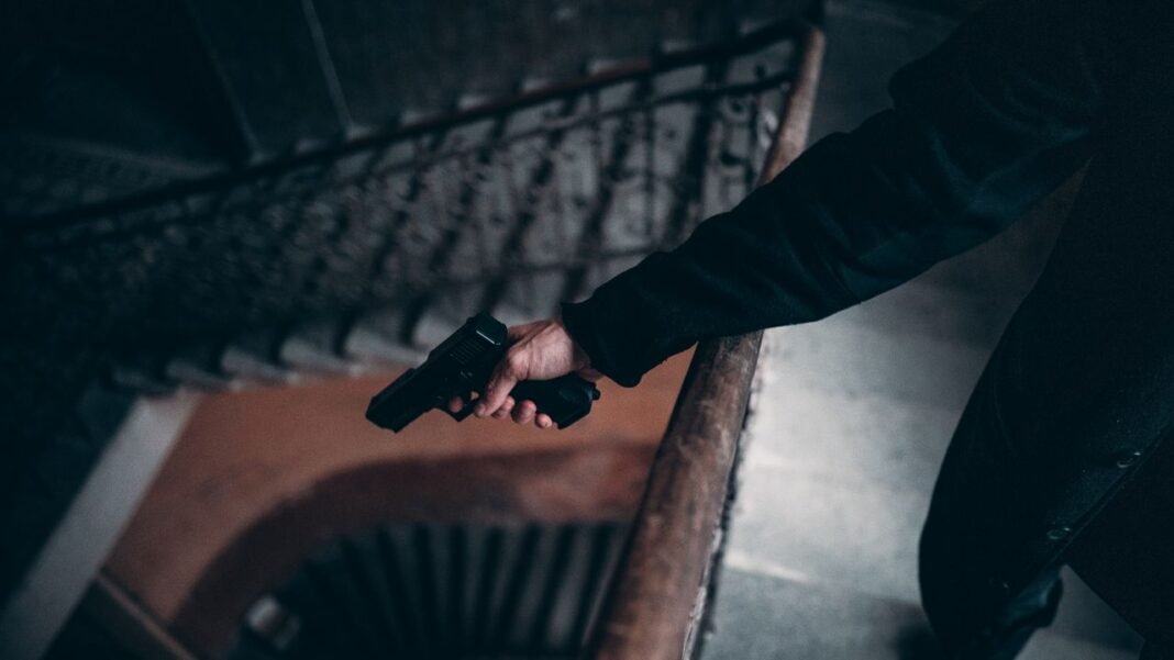 pexels-photo-3156203-3156203 Arm holding a gun on a dimly lit spiral staircase, creating a tense atmosphere.