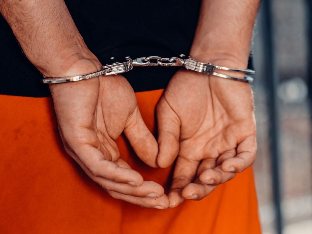 pexels-photo-7785052-7785052 Rear view of handcuffed person in orange uniform, highlighting law enforcement and justice themes.